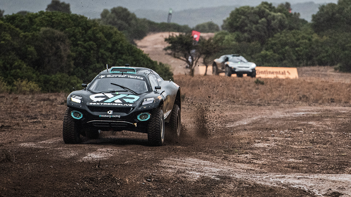 Two off-road vehicles drive through muddy ground in nature.