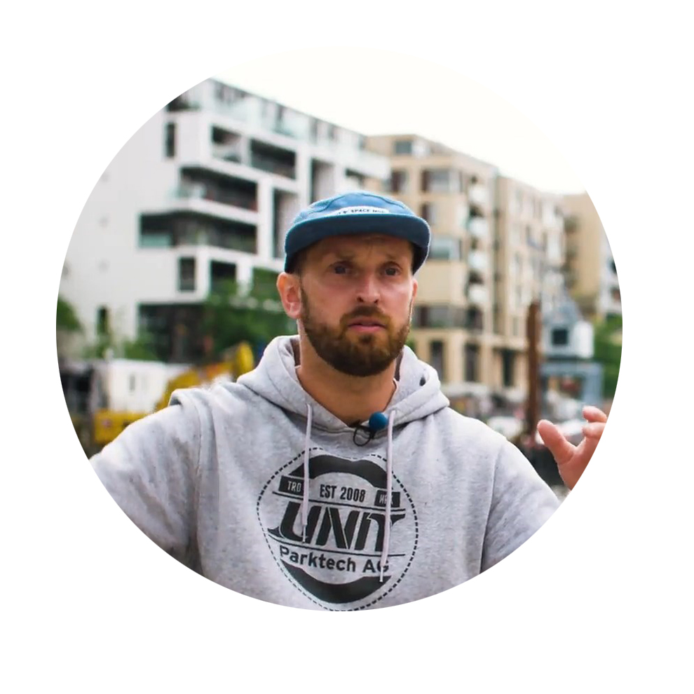 David Vervenne, Track Designer, Unit Parktech A man in a gray hoodie and blue hat speaks in front of modern buildings.