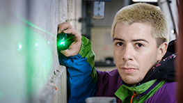 Künstler Roberto Rivadeneira A young man with blonde hair is using a green laser on a wall.