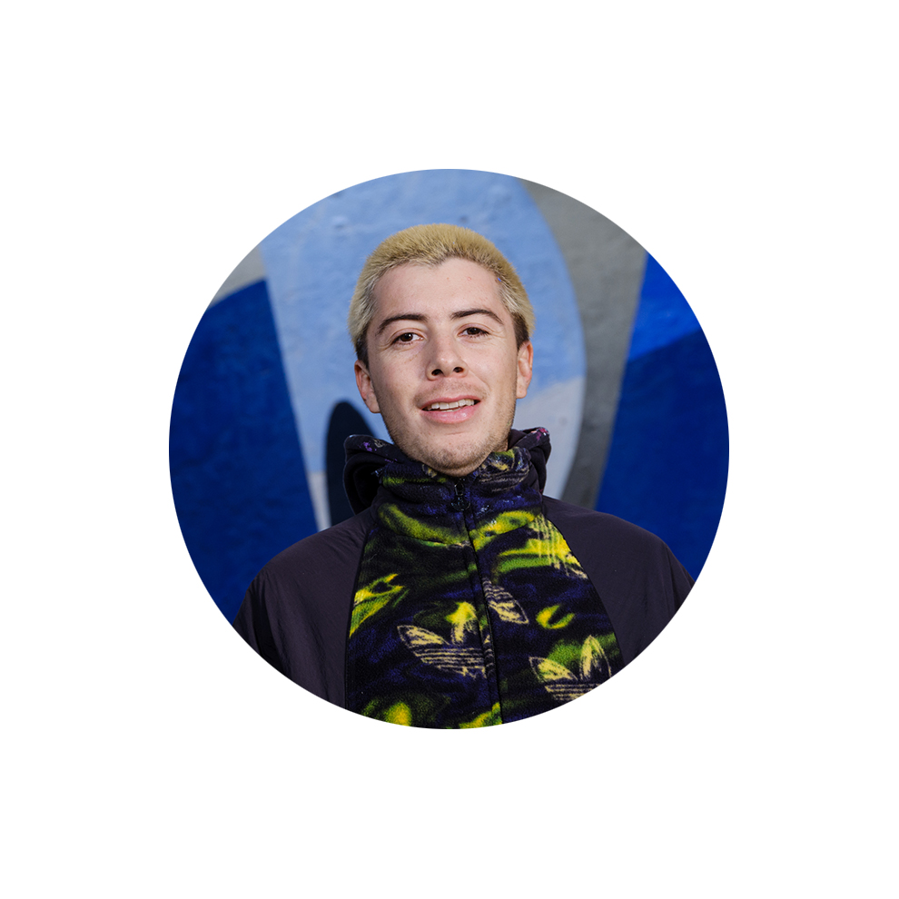 Young man with blonde hair and colorful hoodie in front of a mural background.