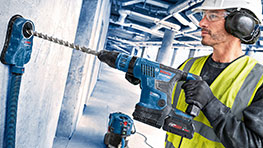 A man wearing hearing protection is drilling with a blue Bosch Professional tool.