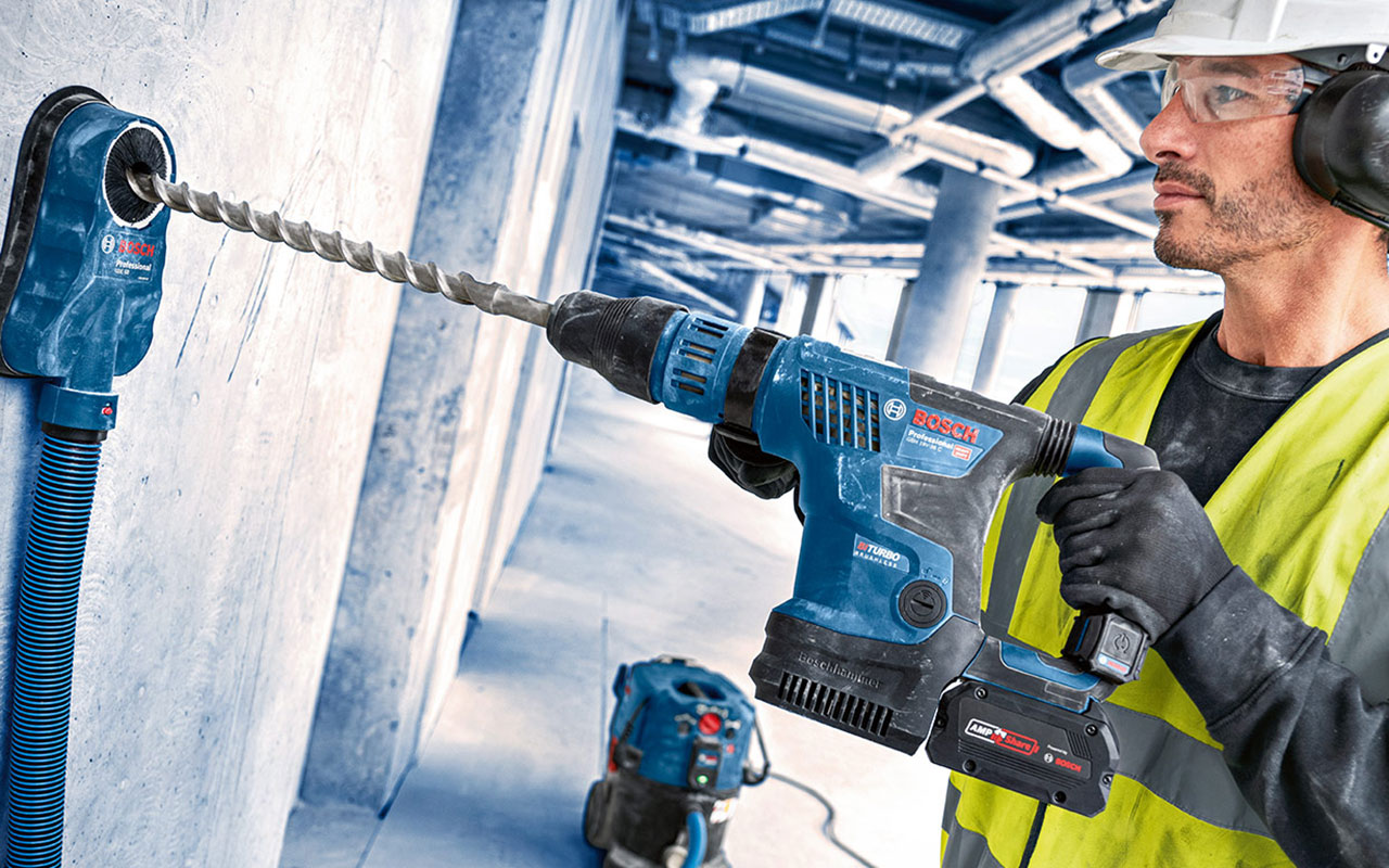 A craftsman with a blue Bosch Professional drill on a wall.