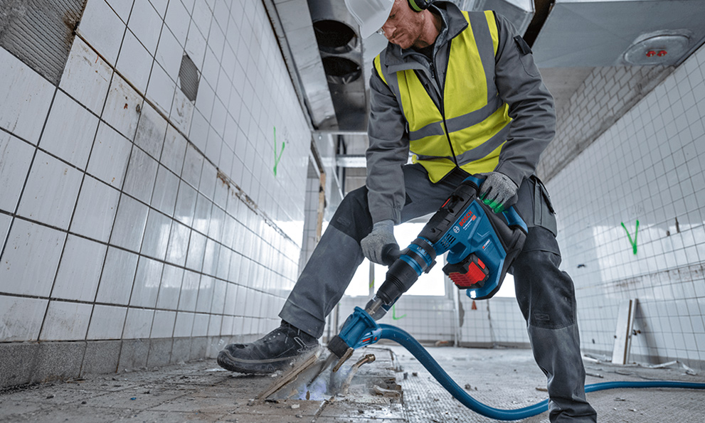 A worker with Bosch tools is breaking tiles in a bright room.