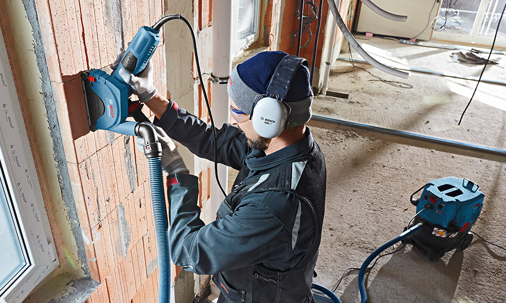 A man wearing hearing protection is using a Bosch Professional tool on a wall.