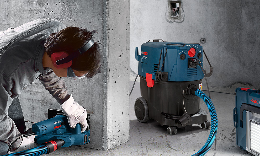 CUTTING CONCRETE WITH WALL CHASERS A craftsman is using a blue Bosch Professional cordless drill on a wall.