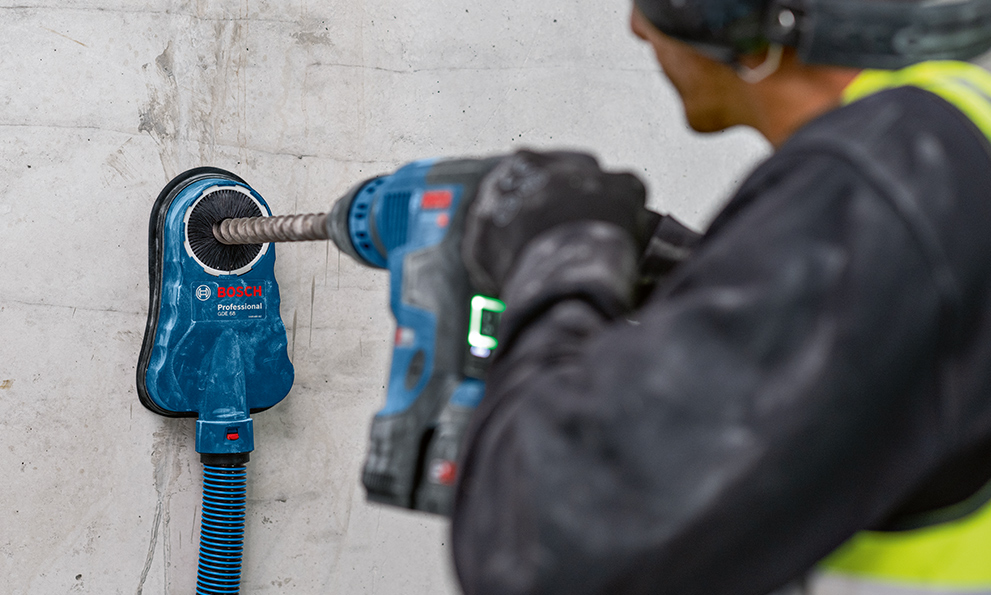 A blue Bosch Professional drill is held against a wall.