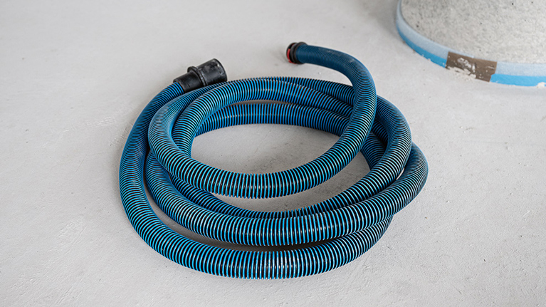 A blue, wavy hose lies on a gray floor.