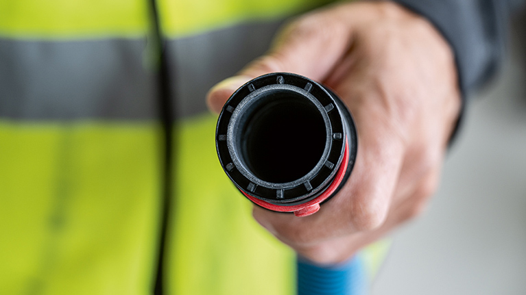 A hand holds a black hose with a red edge in front of a yellow warning vest.