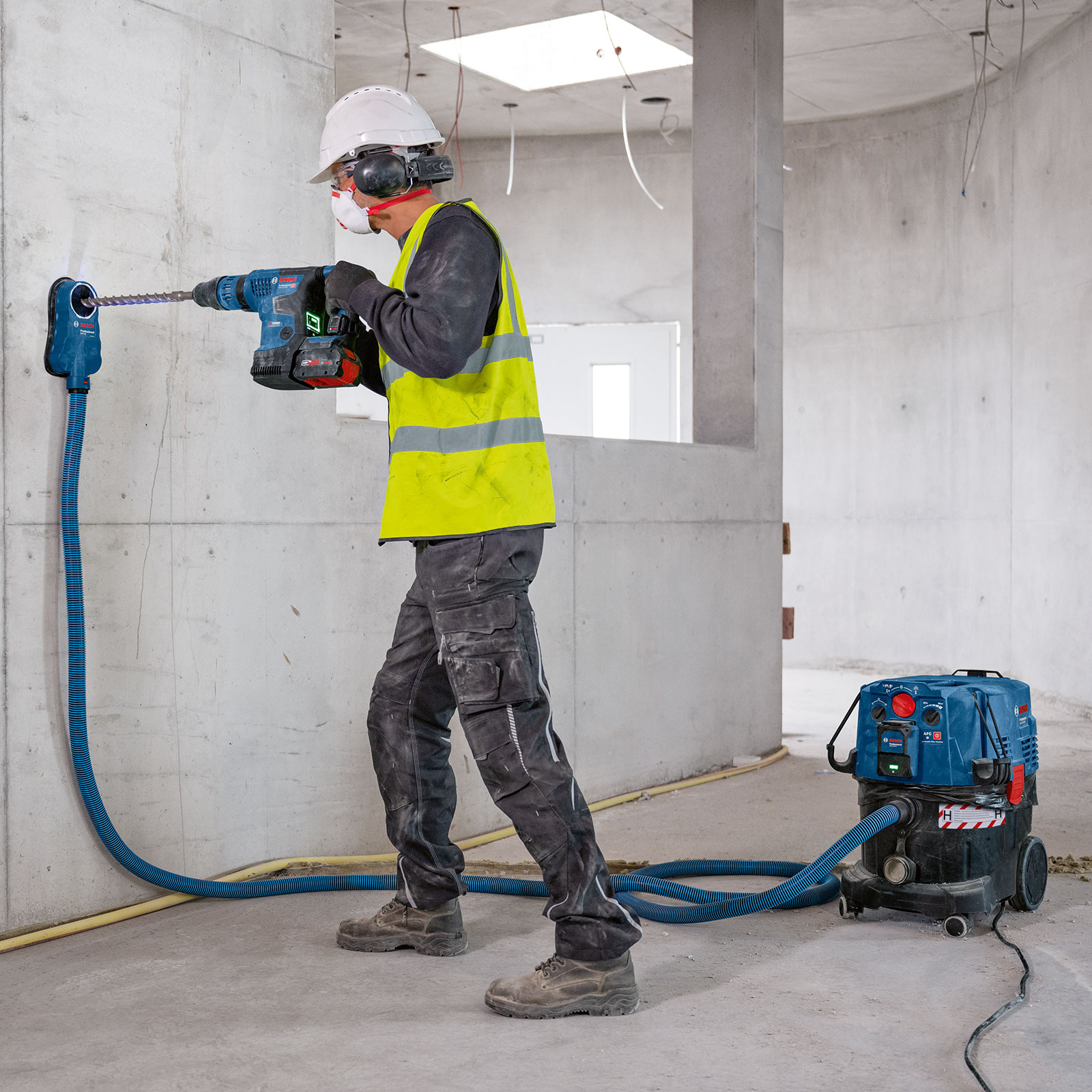 A worker wearing a safety helmet is drilling into a wall with a Bosch tool.