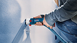 A person is spraying paint with a blue Bosch Professional tool on the wall.