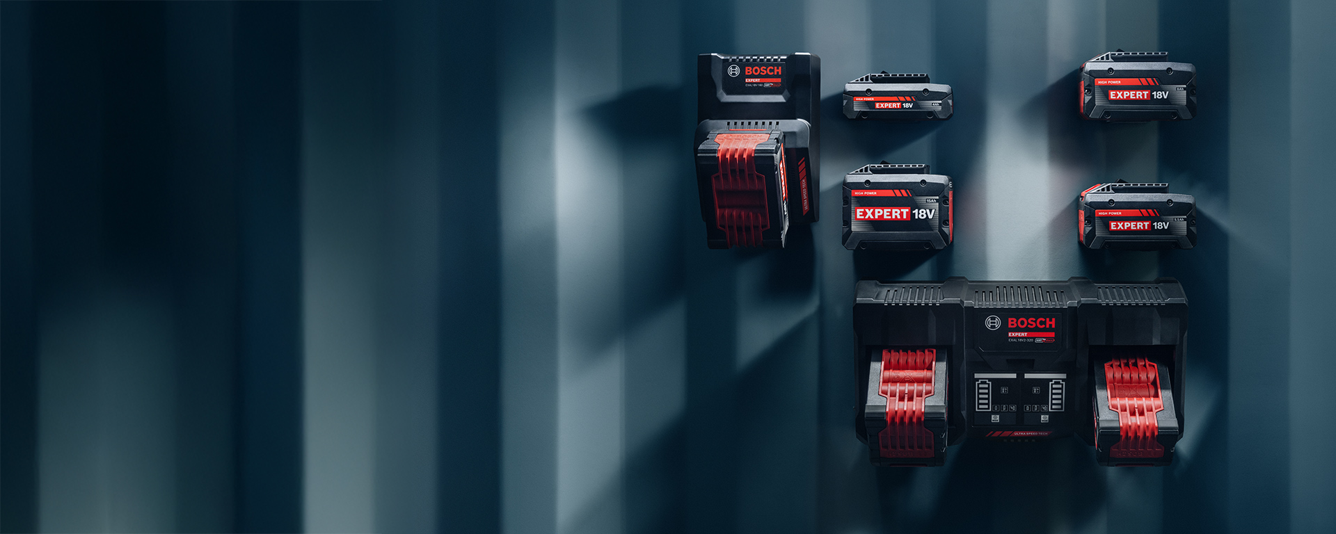 Bosch Expert batteries and chargers arranged on a blue wall.