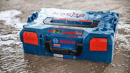 A blue Bosch Expert tool case stands on a wet, gray floor. The case has red latches.