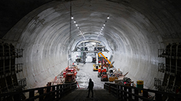 A worker stands in a lit tunnel with construction machinery.