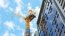 A yellow crane lifts materials next to a modern building under a blue sky.