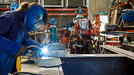 A welder in protective clothing is working on a metal piece.