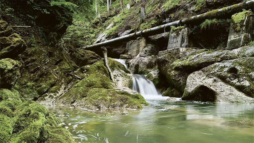 A small waterfall flows over moss-covered rocks into a pond.