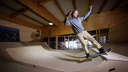 A skateboarder in a wooden skatepark performs a trick.