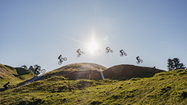 Jed Mildon sets a new record for the world's longest e-bike jump. Five mountain bikers jump over hills in the sunshine.
