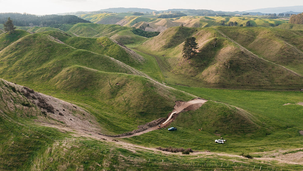 Green, gentle hills under a blue sky with cars in the valley.