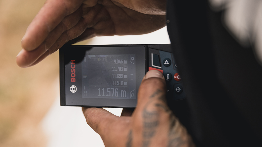 A hand holds a Bosch Professional laser distance measurer with display.
