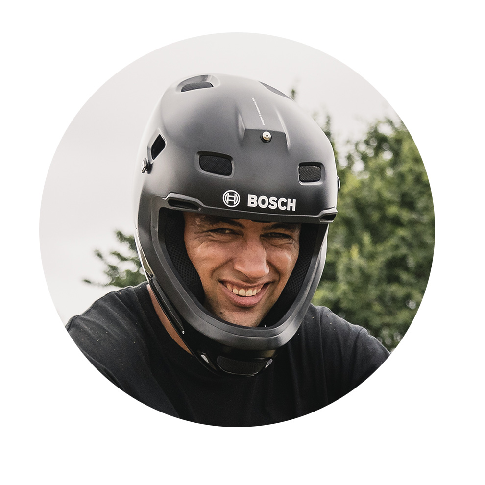 A man with a black Bosch helmet smiles in front of a green background scene.