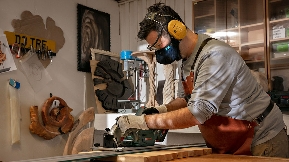 A man wearing safety glasses and hearing protection is working with wood using a Bosch saw.