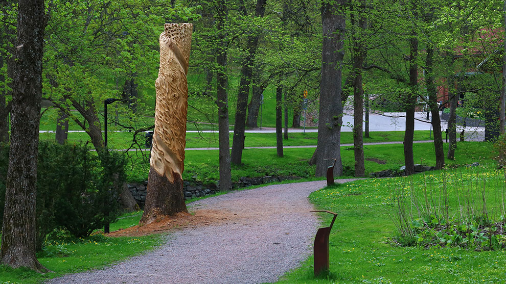 A large wooden sculpture stands in a green park next to a path.
