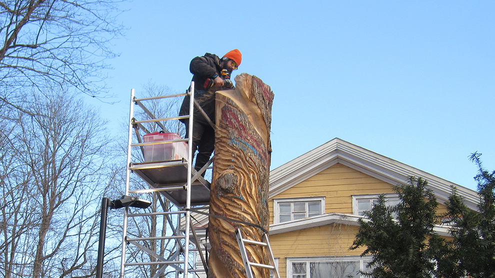 A man with an orange hat is carving on a tree trunk.