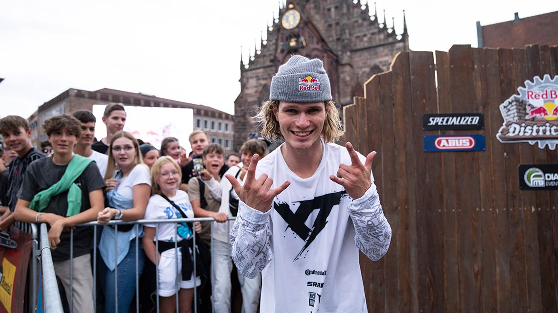 A young man in casual attire poses in front of a crowd.