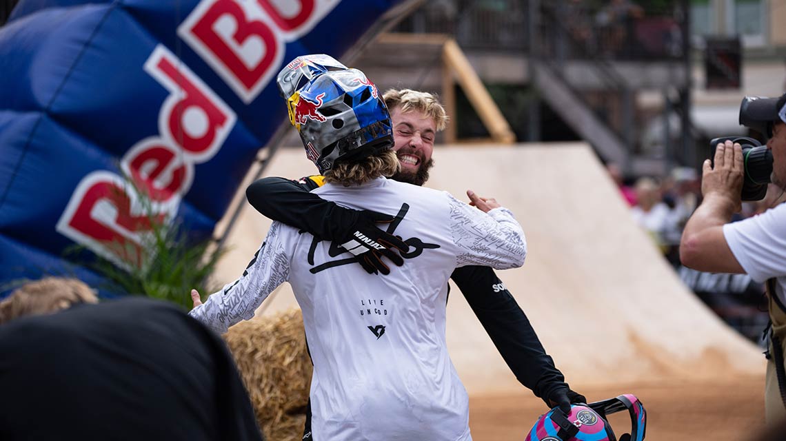 Two men joyfully embrace in front of a Red Bull wall.
