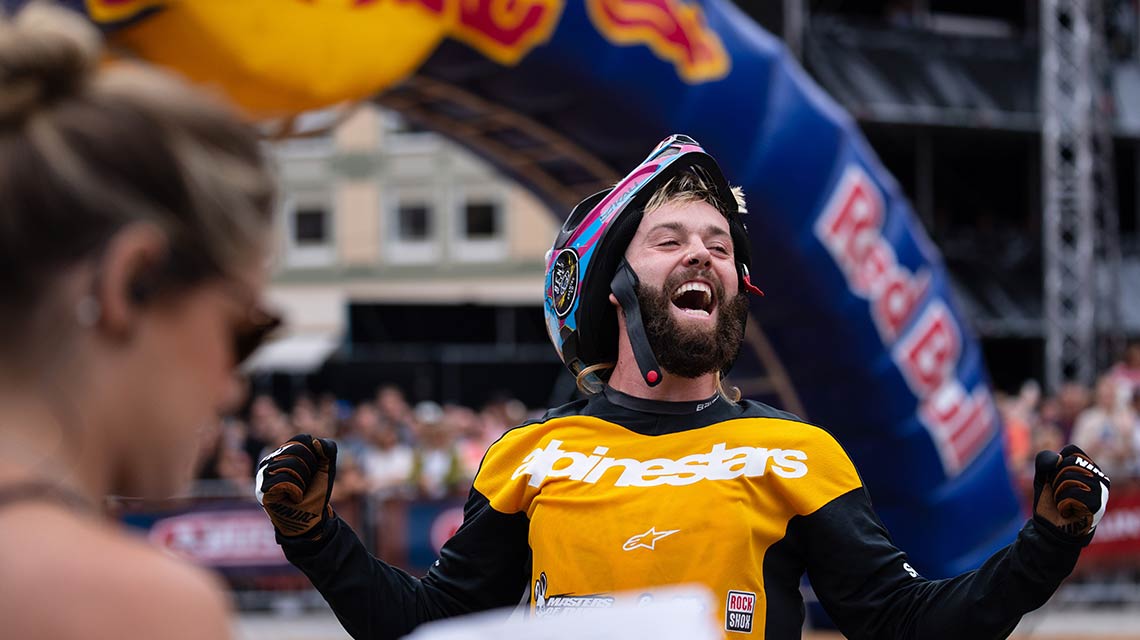 A cheering cyclist in a yellow shirt celebrates in front of an audience.