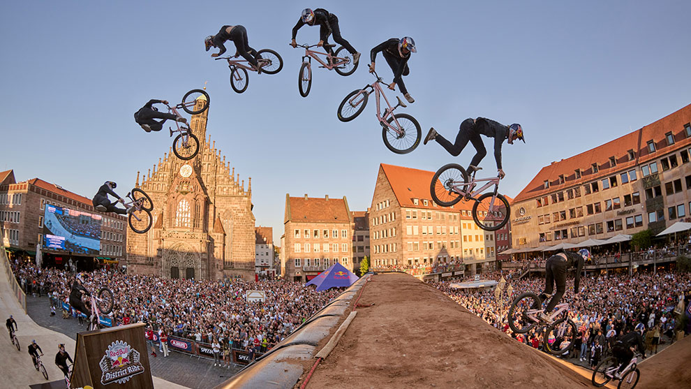 A BMX rider jumps over a ramp in front of a large crowd.