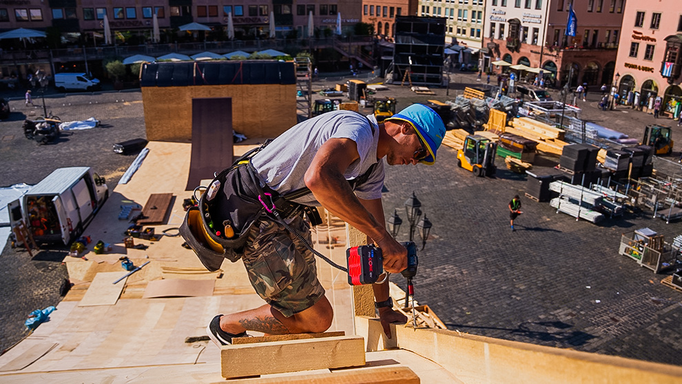 A craftsman with a blue hat is drilling into wood at a construction site.