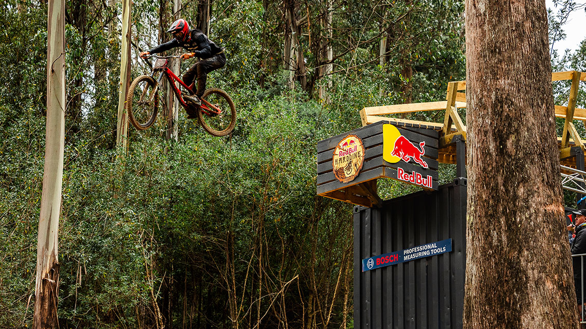 A mountain biker jumps over a wooden ramp in the forest.