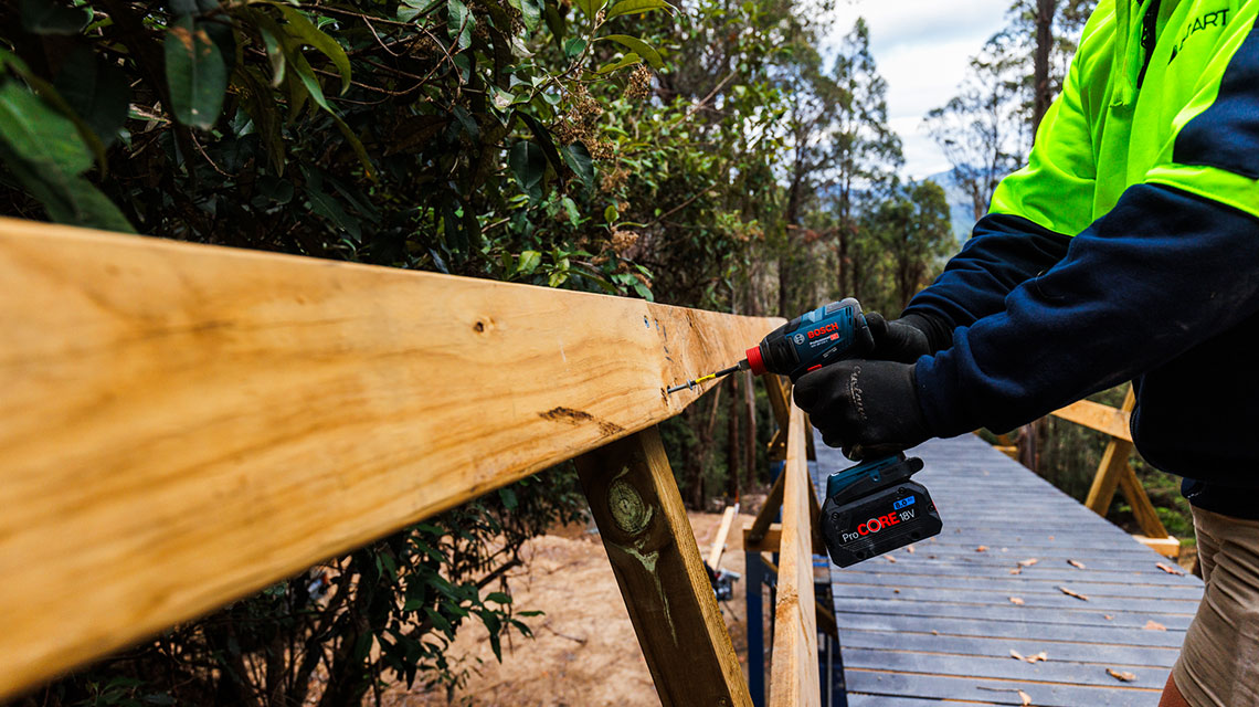 A craftsman is using a Bosch cordless screwdriver to attach a wooden board.