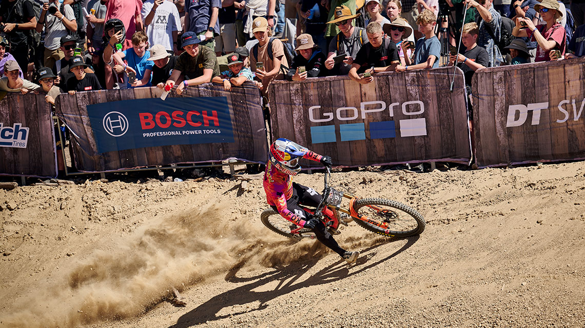 A cyclist in a pink jersey rides through sand, surrounded by spectators.