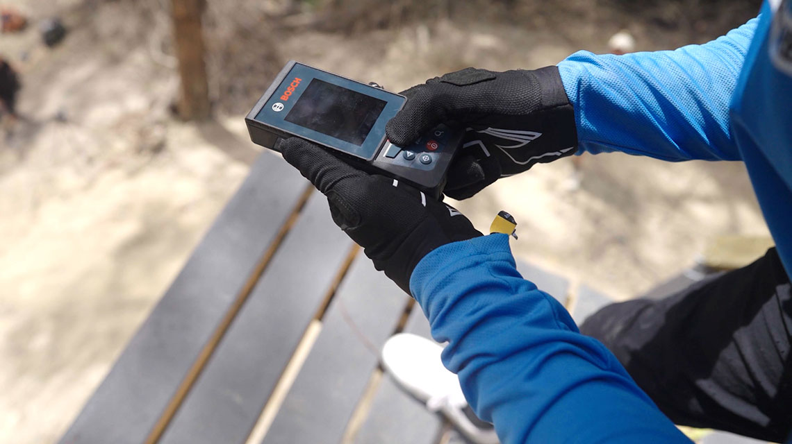 A person in blue clothing holds a Bosch measuring device in their hand.