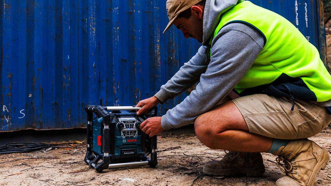A man in a safety vest is adjusting a Bosch subwoofer.