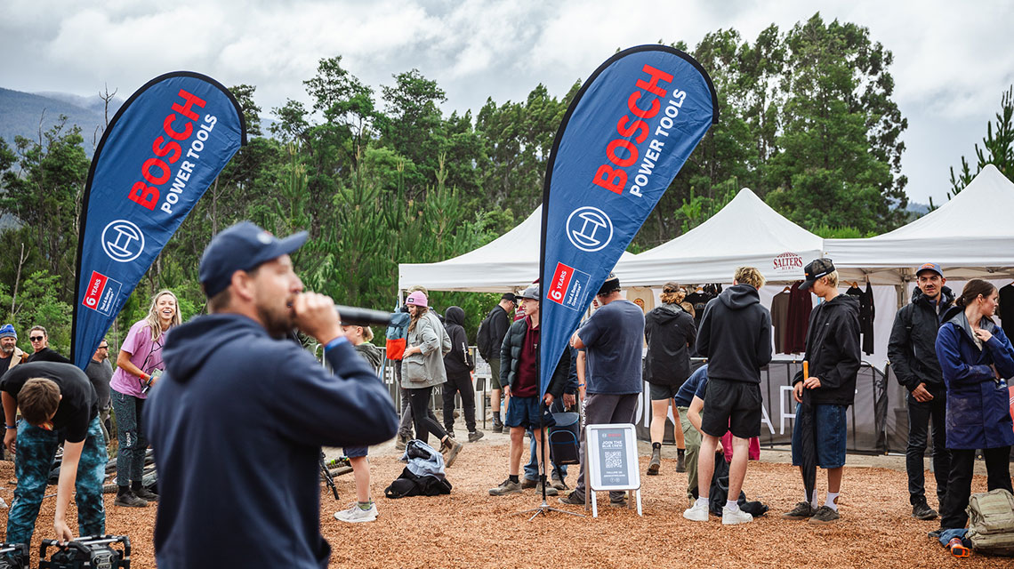 People stand around Bosch Power Tools flags and tents in nature.