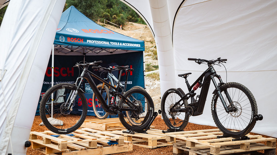 Two black e-bikes are standing on wooden pallets under a Bosch tent.