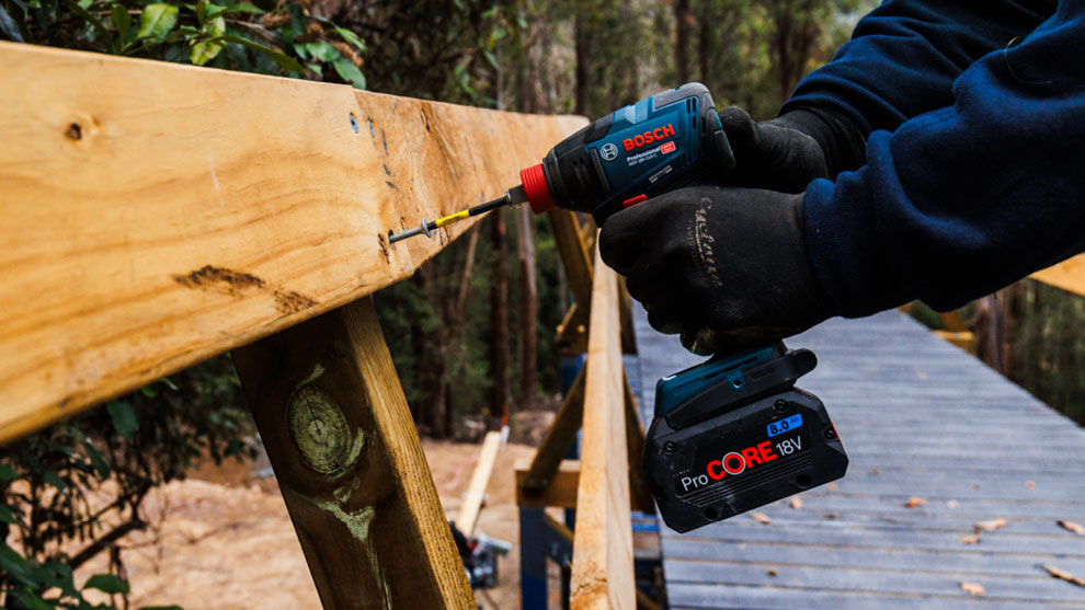 BUILD-UP TILL THE RACE A Bosch Professional cordless screwdriver is being screwed into wood, the surroundings are green.