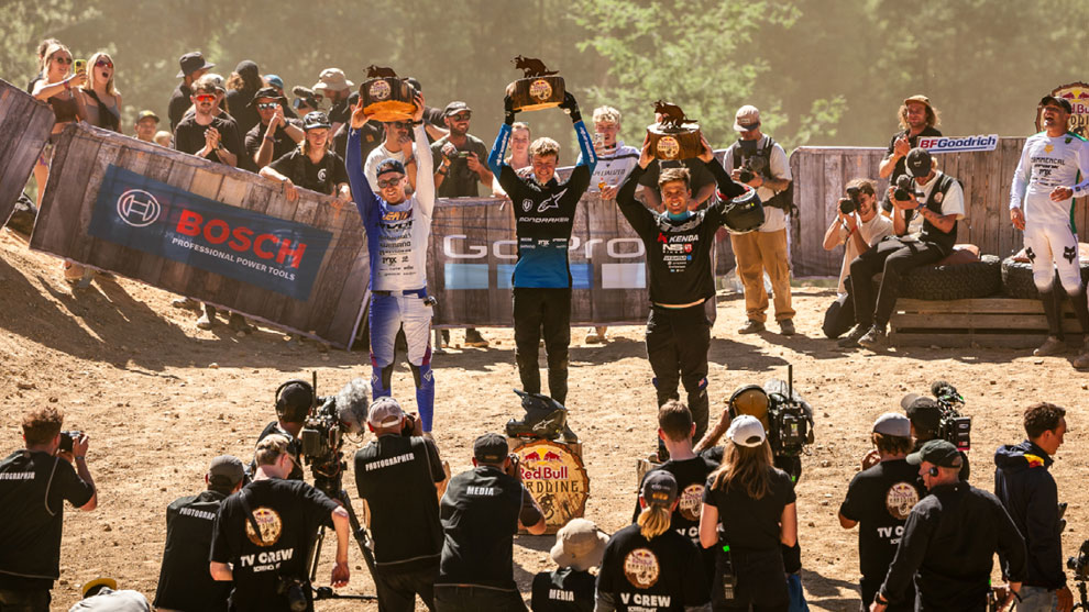 ONLY FOR THE VERY BEST Three winners raise trophies on a podium, surrounded by cheering crowds.