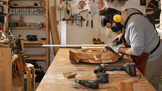 A craftsman is working with wood using a Bosch Professional tool.