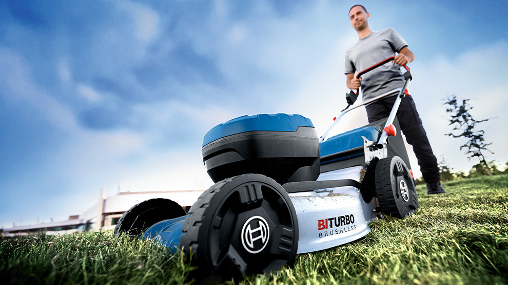 A man is mowing grass with a blue Bosch lawn mower outdoors.